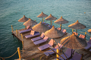 Summer Scene of Umbrella with Sunbeds on Wooden Pier and Ionian Sea in Ksamil. Vacation Lounger...