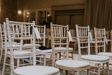 Beige, wooden chiavari chairs set out with placenames for a wedding ceremony