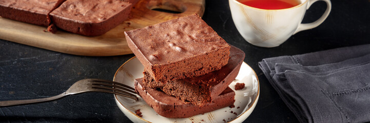 Chocolate brownie with tea panorama, simple coffee cake, on a black slate background