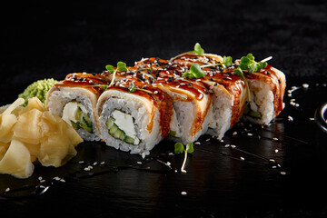 Canada roll with eel and unagi sauce, presented on a black slate with soy sauce and wasabi