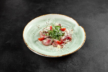 Roast beef carpaccio with Parmesan, arugula, and tomatoes on a speckled turquoise plate