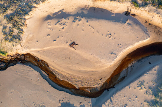 Aerial view of tannin stained creek winding its way over a sandy beach