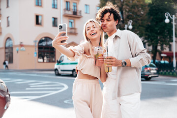 Young smiling beautiful woman and her handsome boyfriend in casual summer clothes. Happy cheerful family. Female having fun. Couple posing in street. Holding and drinking cocktail drink in plastic cup