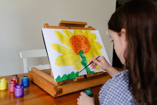 Young girl at home sitting at an easel painting a sunflower