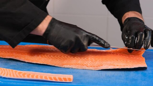 Cutting raw salmon fillet. The cook cuts off the unusable parts of the fish.