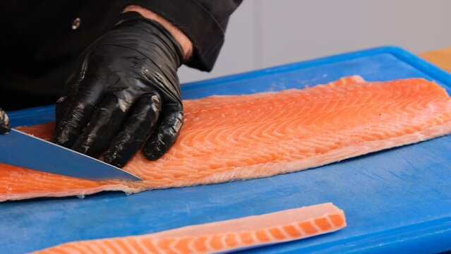 Cutting raw salmon fillet. The cook cuts off the unusable parts of the fish.