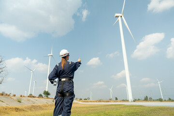 Professional technician woman worker stand in front of wind turbine or windmill and point to the...