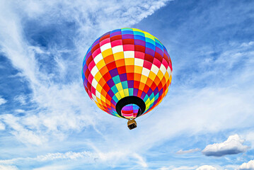 Colorful hot air balloon flying over blue sky with white clouds