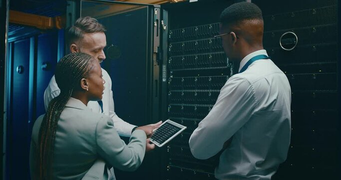 Team in server room with tablet, discussion for engineering and network maintenance for data update. Tech support, men and woman in system administration with digital app for technician in datacenter