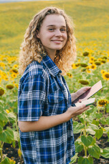 Woman farmer holding tablet gadget investigate yellow blooming sunflower field outdoors. Inspection plantation. Smart agriculture concept. Collecting seeds for