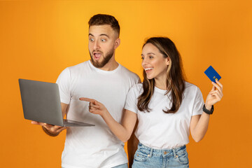 Happy young european man and woman shopaholics in casual use laptop, credit card