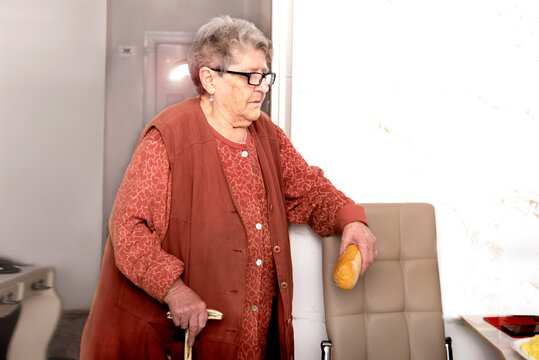 A sweet grandmother with a stick waits for breakfast with a loaf of bread in her hand at a nursing home. Nutrition for the elderly, diet in old age, getting help