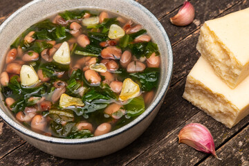 Escarole and pinto beans soup with fried garlic in bowl. Garlic cloves and chunks of parmesan on...
