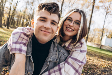 Heterosexual caucasian young loving couple walking outside make selfie in sunny weather, hugging smiling kissing laughing spending time together. Autumn, fall season, orange yellow red maple leaves
