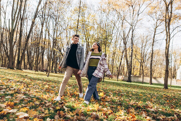 Obraz premium Heterosexual caucasian young loving couple walking outside in the city park in sunny weather, hugging smiling kissing laughing spending time together. Autumn, fall season, orange yellow red maple leav