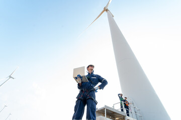 Wide shot professional technician man stand with hold laptop and stand near base of windmill or...