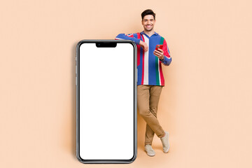 Full length photo of cheerful blogging man using smartphone advertising new day schedule application isolated on beige color background
