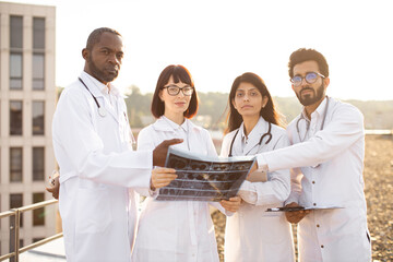 Concept of medicine and health care. Close-up view of four divers confident young adult multicultural doctors discussing patient's CT scan outside the hospital during break.