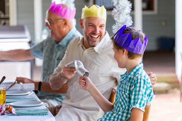Father and son laughing and cracking Christmas crackers together together at Christmas lunch table