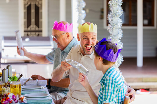 Family laughing and cracking Christmas crackers together at Christmas lunch table