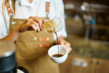 Professional Asian female barista pouring a shot of espresso into a coffee cup close up. 