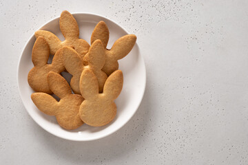 Easter cookies shaped of bunny in white plate on white background. View from above. Copy space. Festive food and kids snacks. Greeting card.