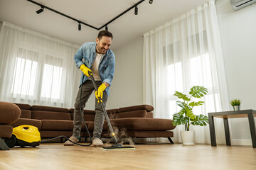 Young man using vacuum cleaner at home - obrazy, fototapety, plakaty