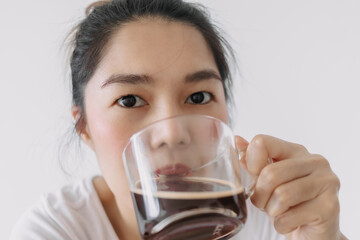 Close up of woman holding and drinking hot coffee mug while looking at camera, isolated over white background wall.