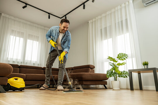 Young Man Using Vacuum Cleaner At Home