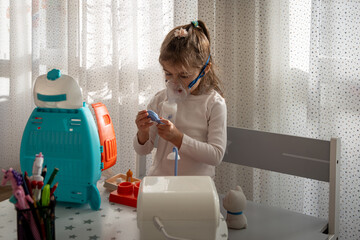 Cute little girl in the mask of an inhaler. Playing with toys. Procedure of inhalation at home. Kid...