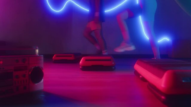 Cropped shot of active sportspeople practicing aerobics steps to boombox music in neon studio