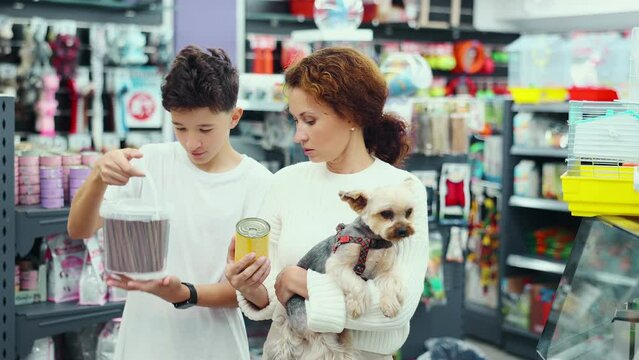 Mother with dog Yorkshire Terrier in her arms and teenage son carefully read composition of product on packaging of dog dry food, examine label, choose healthy food for pet