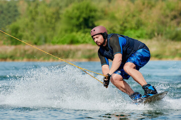 a man on a wakeboard holds onto a winch and sits down before performing a spray trick