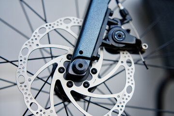 Part of the bicycle's braking system. Grey metal brake disc and brake pads on road bike, close up.