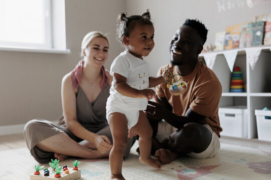 Happy multiracial parents playing with their toddler daughter in nursery.