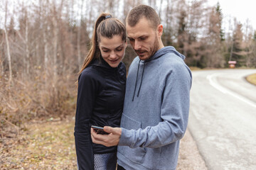Young people checking their fitness progress on smartphone. Two young people checking their fitness progress on a smartphone app after a morning run.