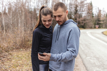 Fototapeta premium Young people checking their fitness progress on smartphone. Two young people checking their fitness progress on a smartphone app after a morning run.