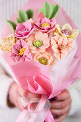 Women's hands hold a bouquet of flowers made from white Belgian chocolate. Close-up.