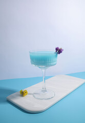 blue cocktail in a transparent glass and decorated with flowers on a light and blue background