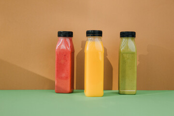 Fruit and vegetable smoothies in transparent plastic bottles. Red, green, orange smoothies on a brown-green background. The concept of healthy eating. Front view