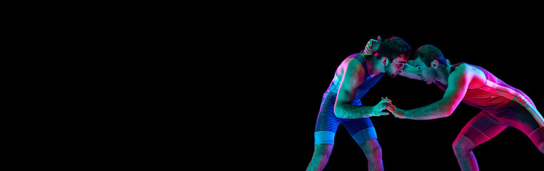 Banner. Two freestyle wrestlers hand fighting in mixed neon lights against black background with...