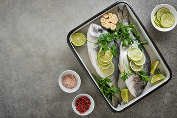 Raw fresh. Fresh raw dorado with lemon, lime, parsley and salt on old grey concrete background ready for cooking. Sea bream, dorado. Seafood, healthy food. Top view. Long banner format.