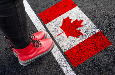 a woman with a boots standing on asphalt next to flag of Canada and border
