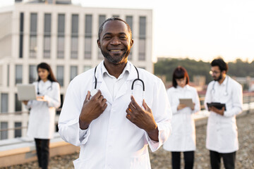 Portrait of confident young African doctor in white lab coat posing on camera with stethoscope and...