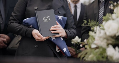 Hands, american flag and bible with a person at a funeral, grieving a loss at a graveyard. War,...