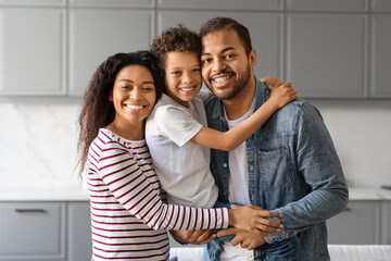 Happy black family with preteen son hugging and smiling in their kitchen