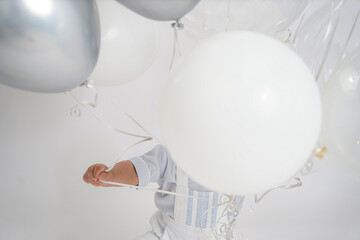 A little kid playing with balloons in the photo shoot in a white background and a cute outfit.     