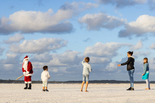 family playing beach cricket with child preparing to bowl to a man dressed as santa