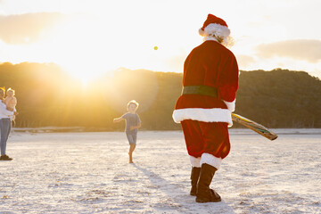 father christmas seen from behind facing a loose ball in beach cricket