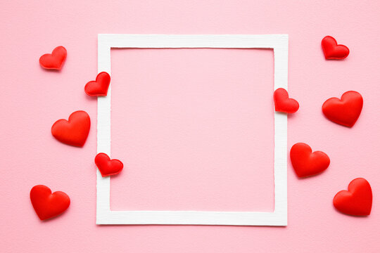 Bright red textile hearts on light pink table background. Pastel color. Love concept. Top view. Empty place for lovely, emotional, sentimental text, quote or sayings in white frame. Closeup.